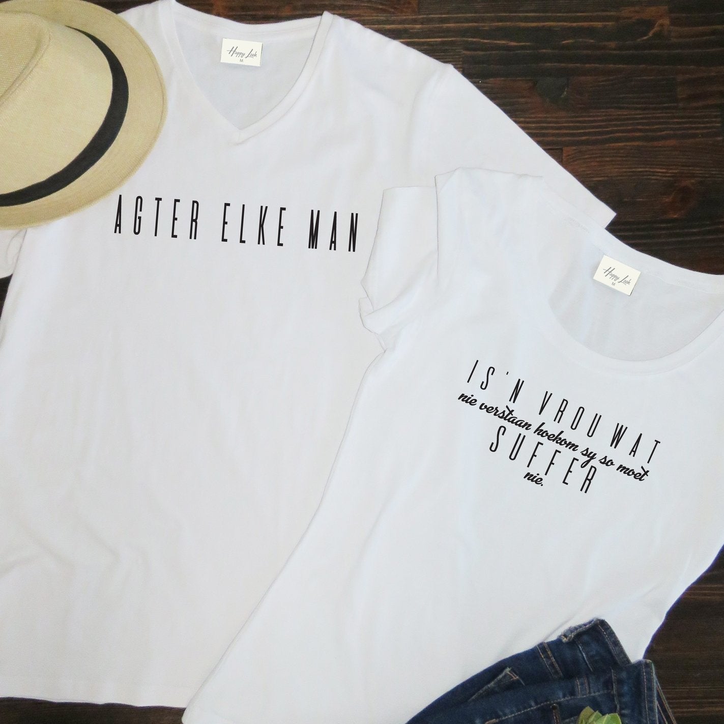 Matching Afrikaans Couple's T-Shirts "Agter Elke Man..." (Behind Every Man) from Happy Look | South Africa – Two white t-shirts with black text in a humorous style. The V-neck men's shirt reads: "AGTER ELKE MAN" and the women's shirt reads: "IS 'N VROUW WAT nie verstaan hoekom sy so moet SUFFER nie" (is a woman who doesn't understand why she has to suffer so much).