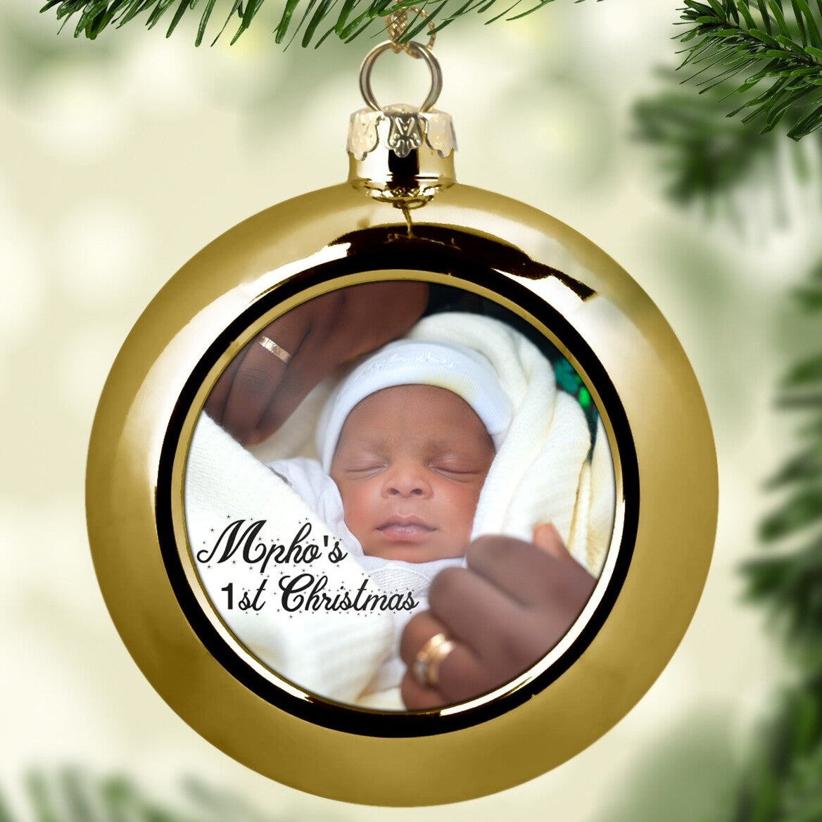 Custom "Mpho's 1st Christmas" Bauble (Gold) from Happy Look | South Africa – A glossy gold Christmas ornament hanging from a tree. The center displays a close-up photo of a sleeping baby, Mpho, with the text "Mpho's 1st Christmas" overlaid in black script.