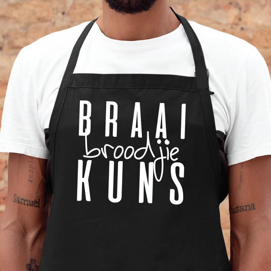 Personalised apron from Happy Look | South Africa – A trendy black apron featuring "BRAAI broodjie KUNS" in artistic fonts. Perfect for creative cooking sessions and braai events, and customisable for every chef. A thoughtful gift that brings joy and lasting memories. Shop now!