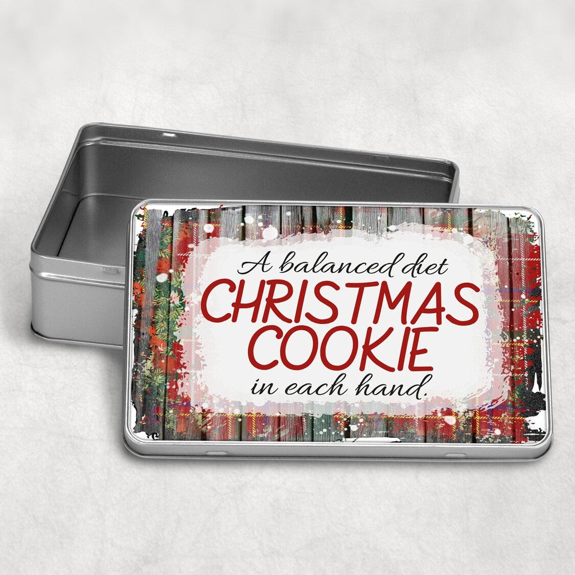 Rectangular Christmas Cookie Tin "A balanced diet CHRISTMAS COOKIE in each hand" from Happy Look | South Africa – A silver rectangular tin with its lid open, featuring a humorous text design over a rustic wood and red tartan background. The text reads: "A balanced diet CHRISTMAS COOKIE in each hand."