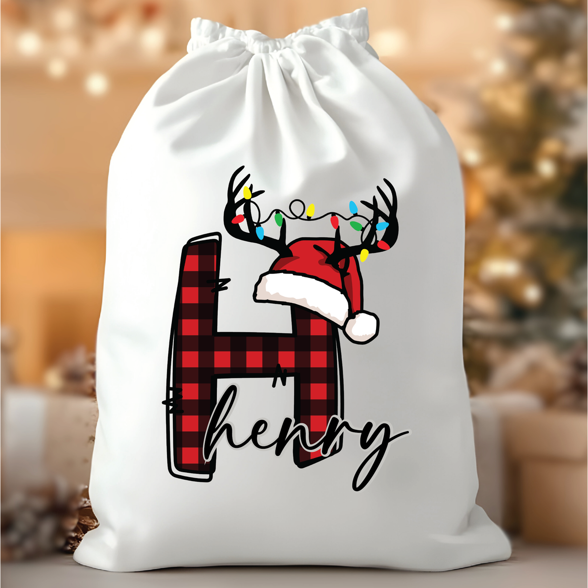 Personalized Initial Santa Sack "Henry" Buffalo Plaid Design from Happy Look | South Africa – A large white drawstring Christmas gift bag featuring a distressed buffalo plaid initial 'H' and a reindeer antler design decorated with Christmas lights and a Santa hat, personalized for "Henry."