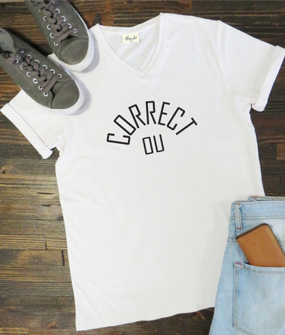 White t-shirt with 'CORRECT DU' text on a wooden surface with shoes and jeans.