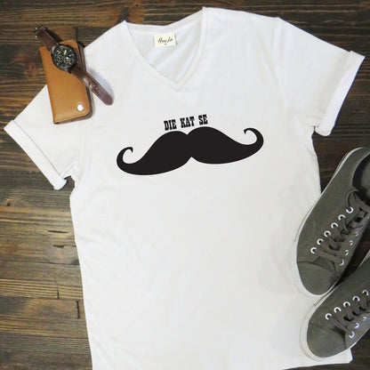 White t-shirt with a black mustache graphic and text on a wooden surface with shoes and a watch.