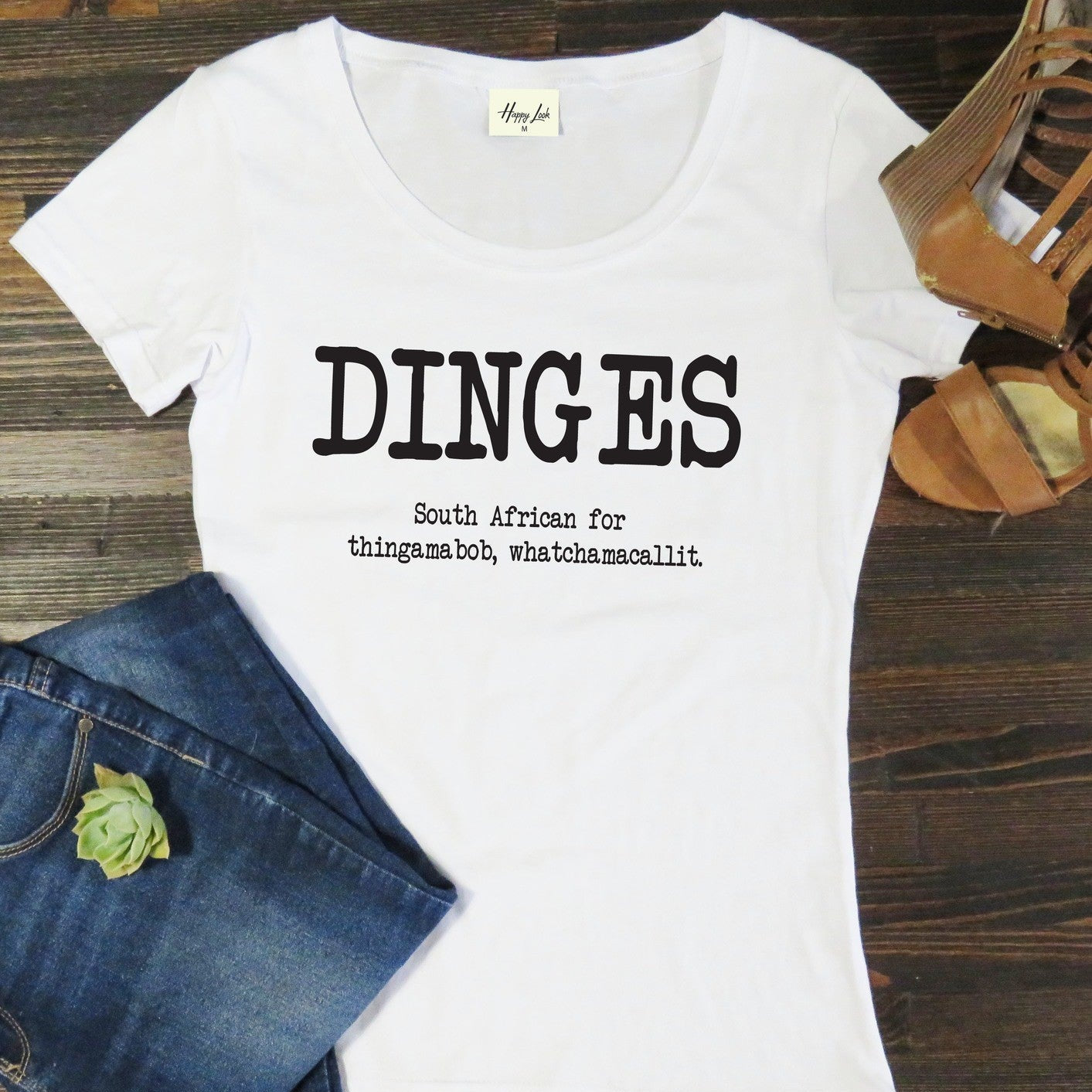 White t-shirt with 'DINGES' text on a wooden surface with jeans and sandals.