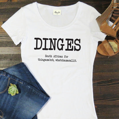 White t-shirt with 'DINGES' text on a wooden surface with jeans and sandals.