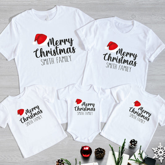 Personalised Family Christmas T-Shirts from Happy Look | South Africa – Matching white t-shirts and baby grow featuring “Merry Christmas Smith Family” with a festive red Santa hat. A joyful family outfit for the holidays, perfect for Christmas photos, family gatherings, and festive gifting. Celebrate the season in style with custom Christmas apparel that spreads love and cheer.