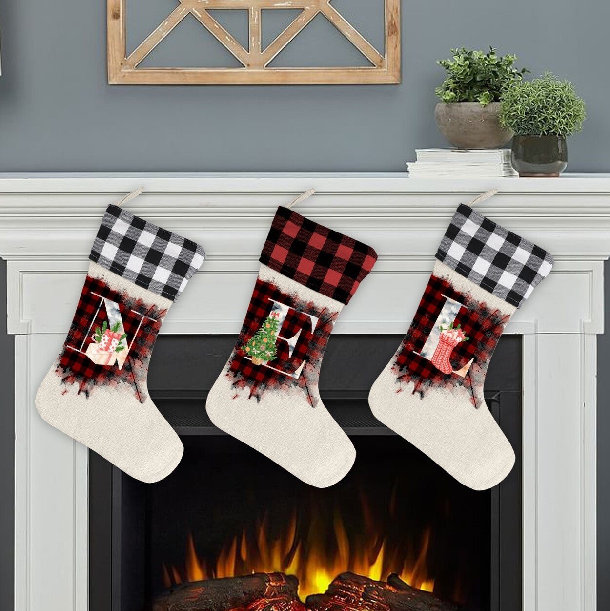 Initial Picture Frame Christmas Stockings from Happy Look | South Africa – Three hanging stockings on a mantel with cream bodies and buffalo plaid cuffs (alternating black and red). Each features a distressed white frame containing a large initial (A, E), an image of a Christmas object (present, tree, stocking), and plaid texture.
