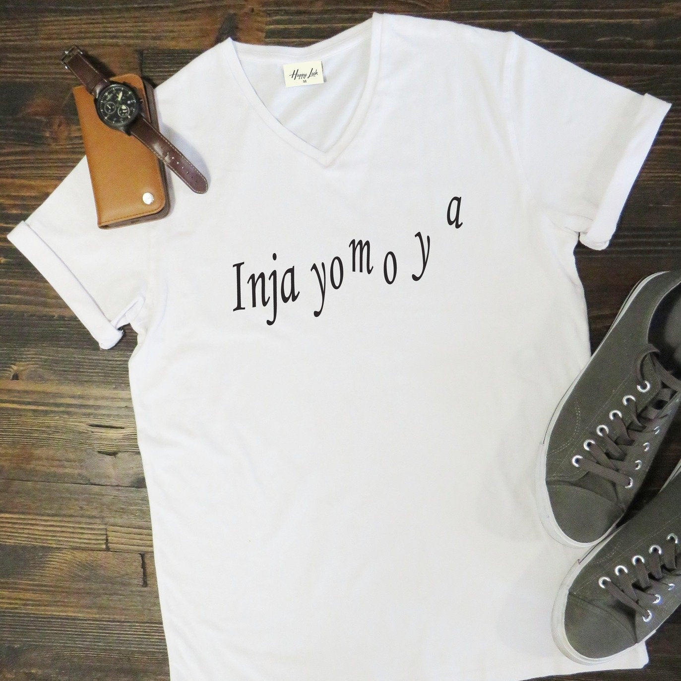 White t-shirt with text on a wooden surface with shoes and a watch.