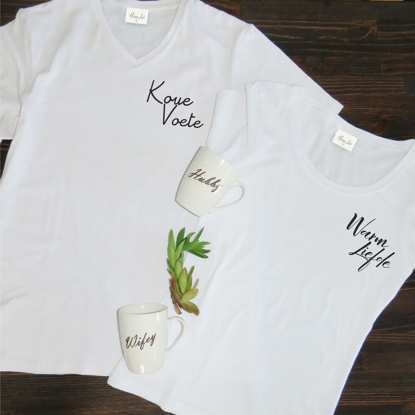 A matching couple’s T-shirt set with one white shirt printed “Koue Voet” and the other “Warm Liefde” in bold, stylish lettering. The set is displayed side by side, symbolising a playful and loving connection between two people.
