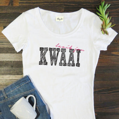 White t-shirt with 'Laai jou KWAAI' text on a wooden surface with jeans and a mug.