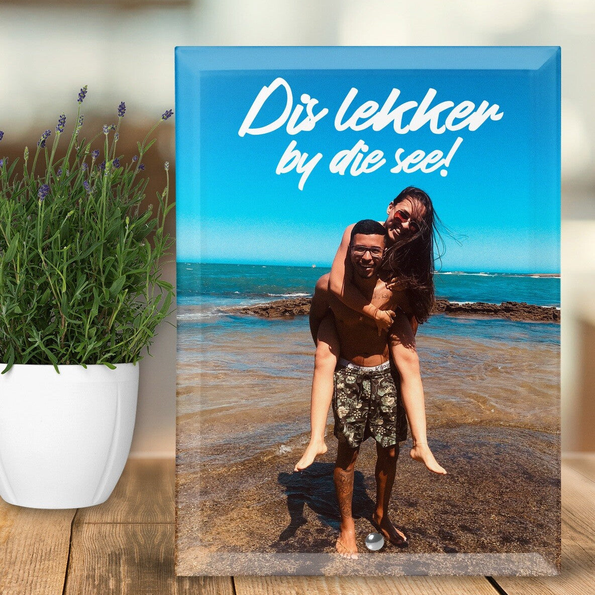 Custom Photo Glass Block "Dis lekker by die see!" (It is nice by the sea!) from Happy Look | South Africa – A rectangular glass block featuring a couple on a beach with the man giving the woman a piggyback ride, overlaid with the Afrikaans text "Dis lekker by die see!" against a bright blue sky