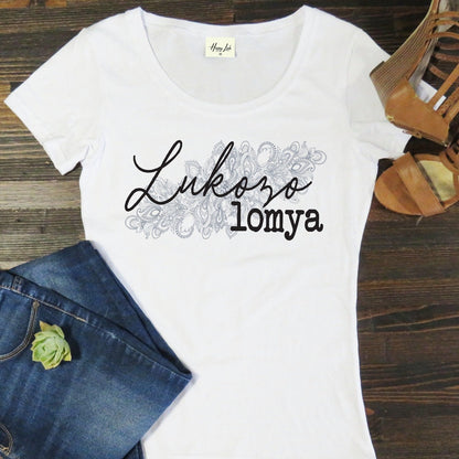White t-shirt with 'Lukozo lomya' text on a wooden surface with jeans and sandals.