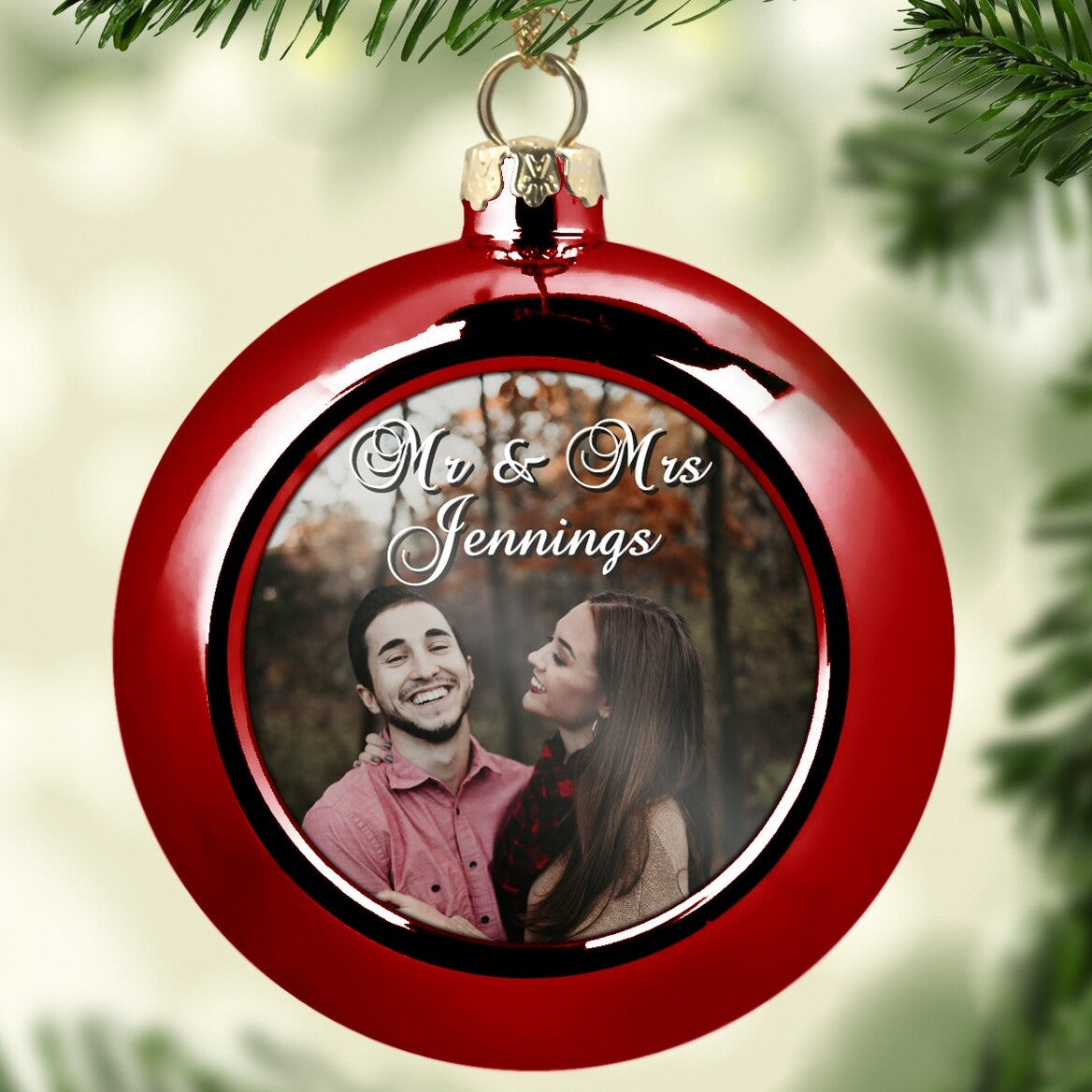 Custom Couple Photo Christmas Bauble "Mr & Mrs Jennings" from Happy Look | South Africa – A bright red glossy Christmas ornament hanging from a tree. The center displays a photo of a smiling couple outdoors, overlaid with the white script "Mr & Mrs Jennings." Ideal for newlyweds.