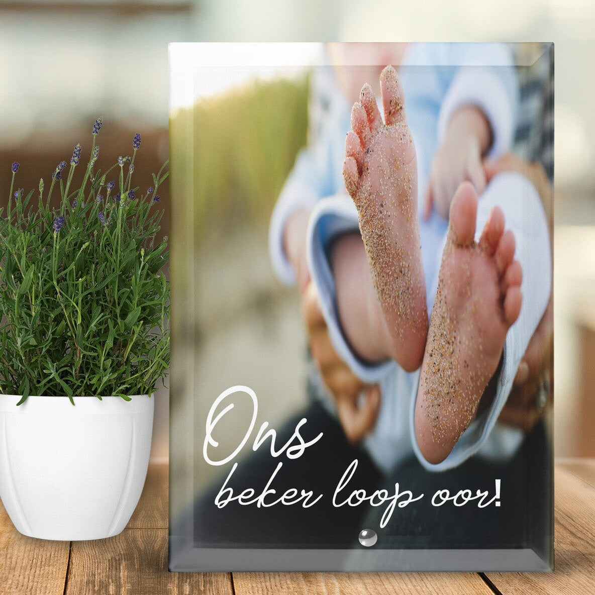 Glass photo frame with baby feet and text on a wooden surface with a plant.