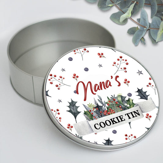 Round Personalized Christmas Cookie Tin "Nana's COOKIE TIN" from Happy Look | South Africa – An open round silver tin with its lid leaning against it. The lid features a watercolor design of holly and berries around the script text "Nana's" and a banner with "COOKIE TIN."