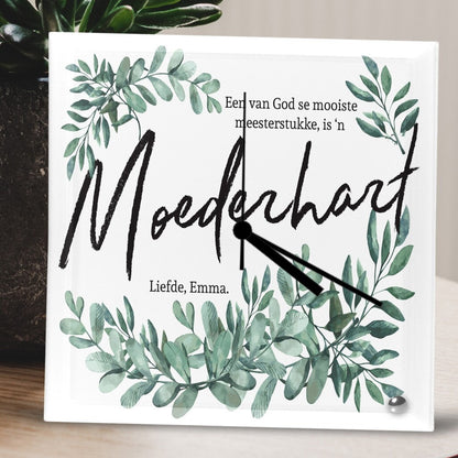 Square Glass Clock featuring a green leafy design on a wooden surface. The text reads, 'Een van God se mooiste meesterstukke, is 'n Moederhart. Liefde, Emma.' A warm and heartfelt message. Personalised Square Glass Clock from Happy Look | South Africa – A beautiful home decor piece with a unique, nature-inspired design. Perfect for Mother's Day, anniversaries, or special occasions and customisable with personal messages. A thoughtful gift that brings joy and lasting memories. Shop now!