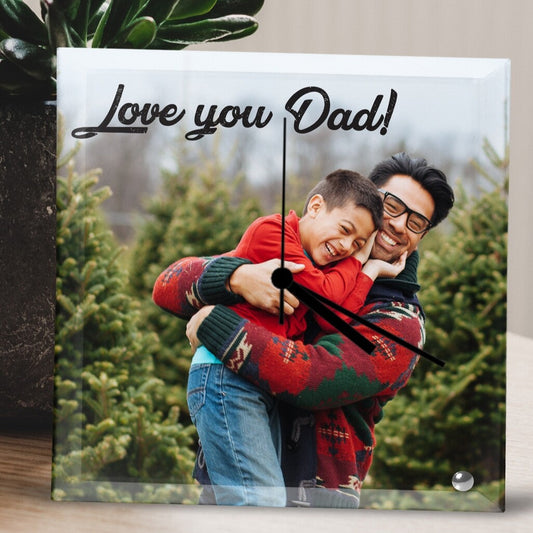 Square Glass Photo Clock displaying a joyful father and son hugging, both in colorful sweaters, surrounded by trees. The text reads, 'Love you Dad!' creating a joyful and warm mood. Personalised Square Glass Clock from Happy Look | South Africa – A heartwarming photo clock that captures cherished moments. Perfect for Father's Day, birthdays, or family celebrations, and customisable with your own personal message. A thoughtful gift that brings joy and lasting memories. Shop now!