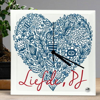 Personalised Square Glass Clock from Happy Look | South Africa – Elegant square glass clock featuring a blue floral heart design on a white background. Black clock hands point to the time, with red cursive text reading "Liefde, PJ." Perfect for anniversaries, weddings, or romantic gestures, and customisable with a special message. A thoughtful gift that brings joy and lasting memories. Shop now!
