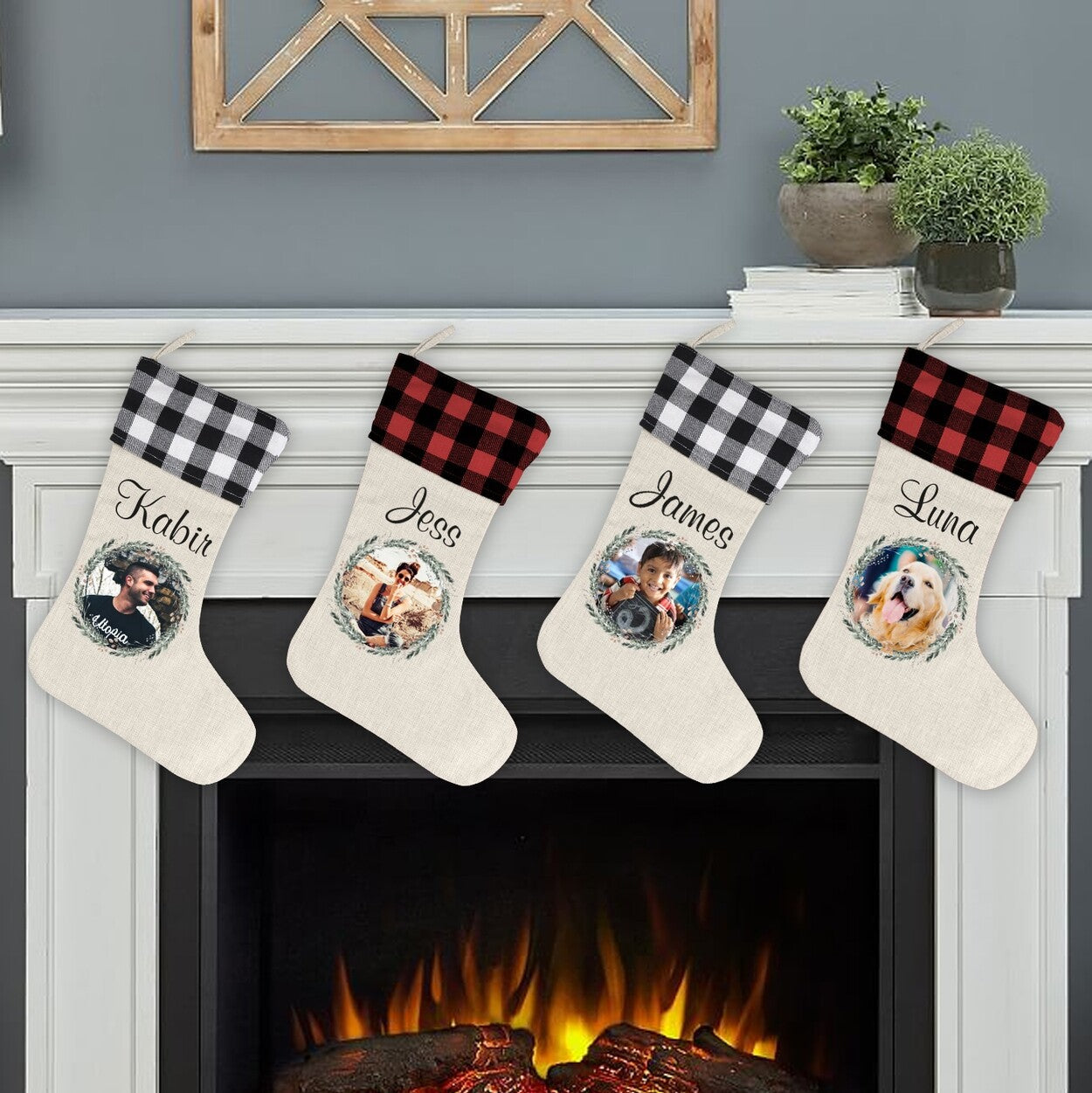Personalised Photo Christmas Stockings from Happy Look | South Africa – Four hanging stockings on a mantel with cream bodies and buffalo plaid cuffs (alternating black and red). Each stocking features a wreath-framed photo of a person or pet and a personalized name: "Kabir," "Jess," "James," and "Luna."
